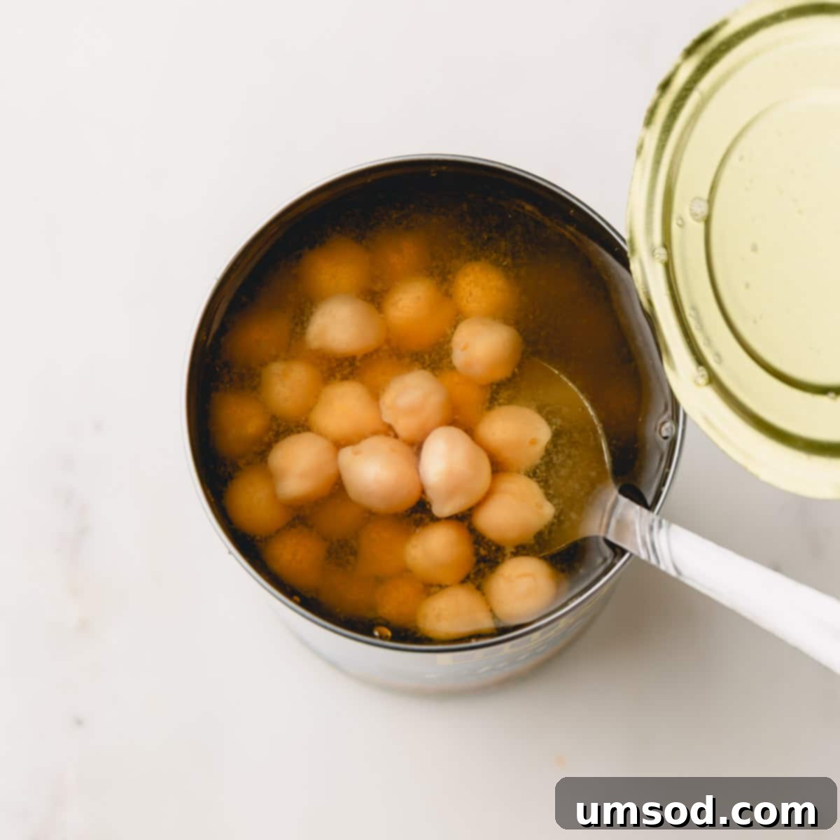 A spoon dipping into a can of chickpeas, illustrating the available aquafaba liquid.
