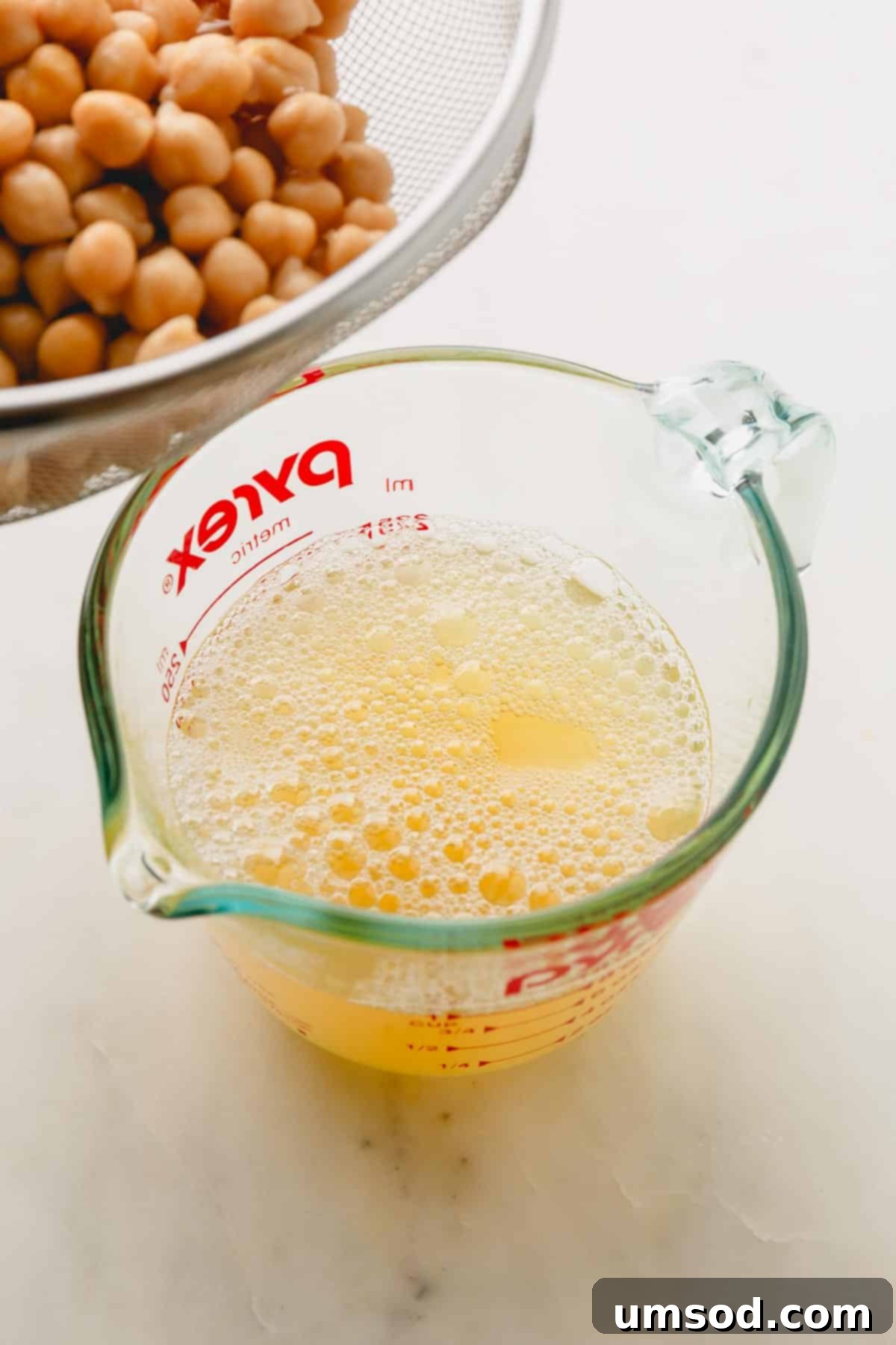 Chickpea water being meticulously drained into a liquid measuring cup.
