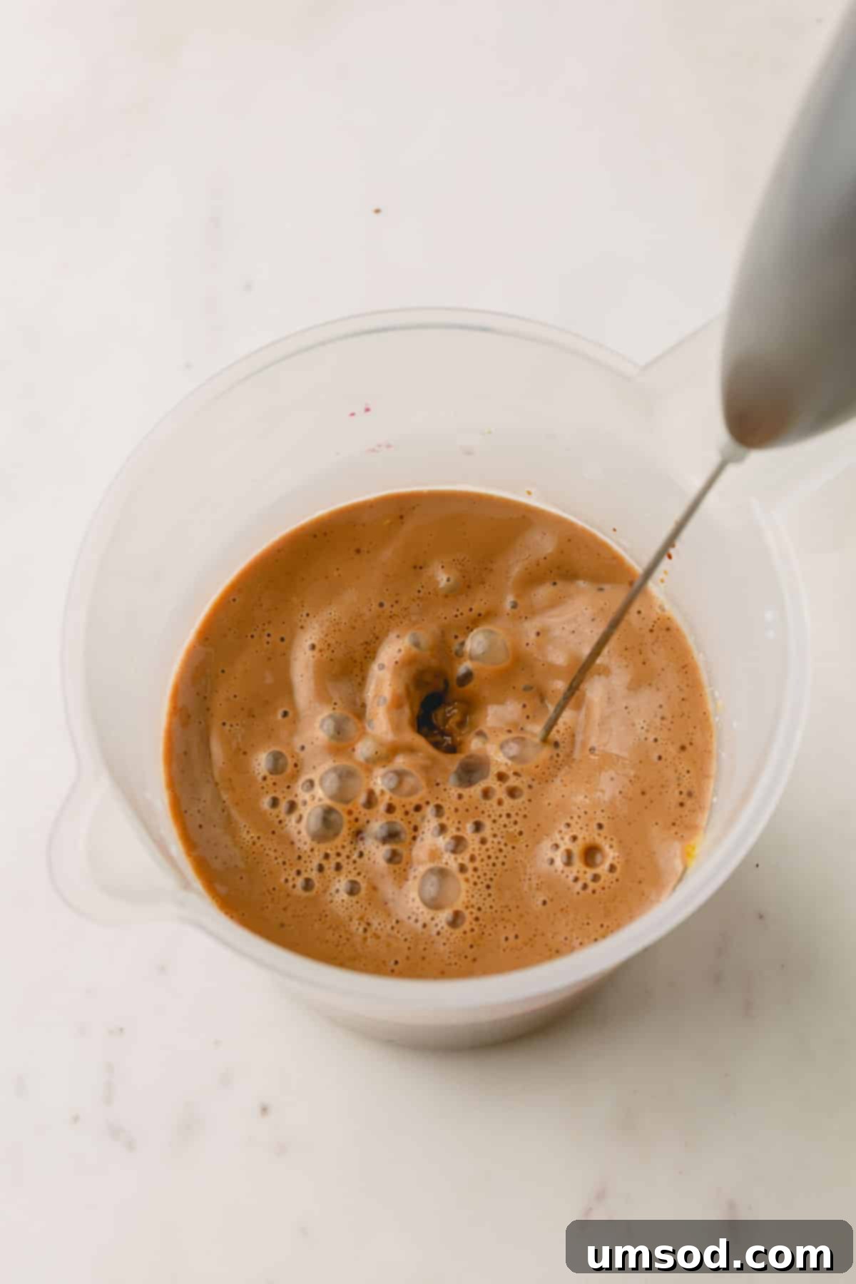 Pistachio latte ingredients being combined in a liquid measuring cup with a milk frother, illustrating the blending process.