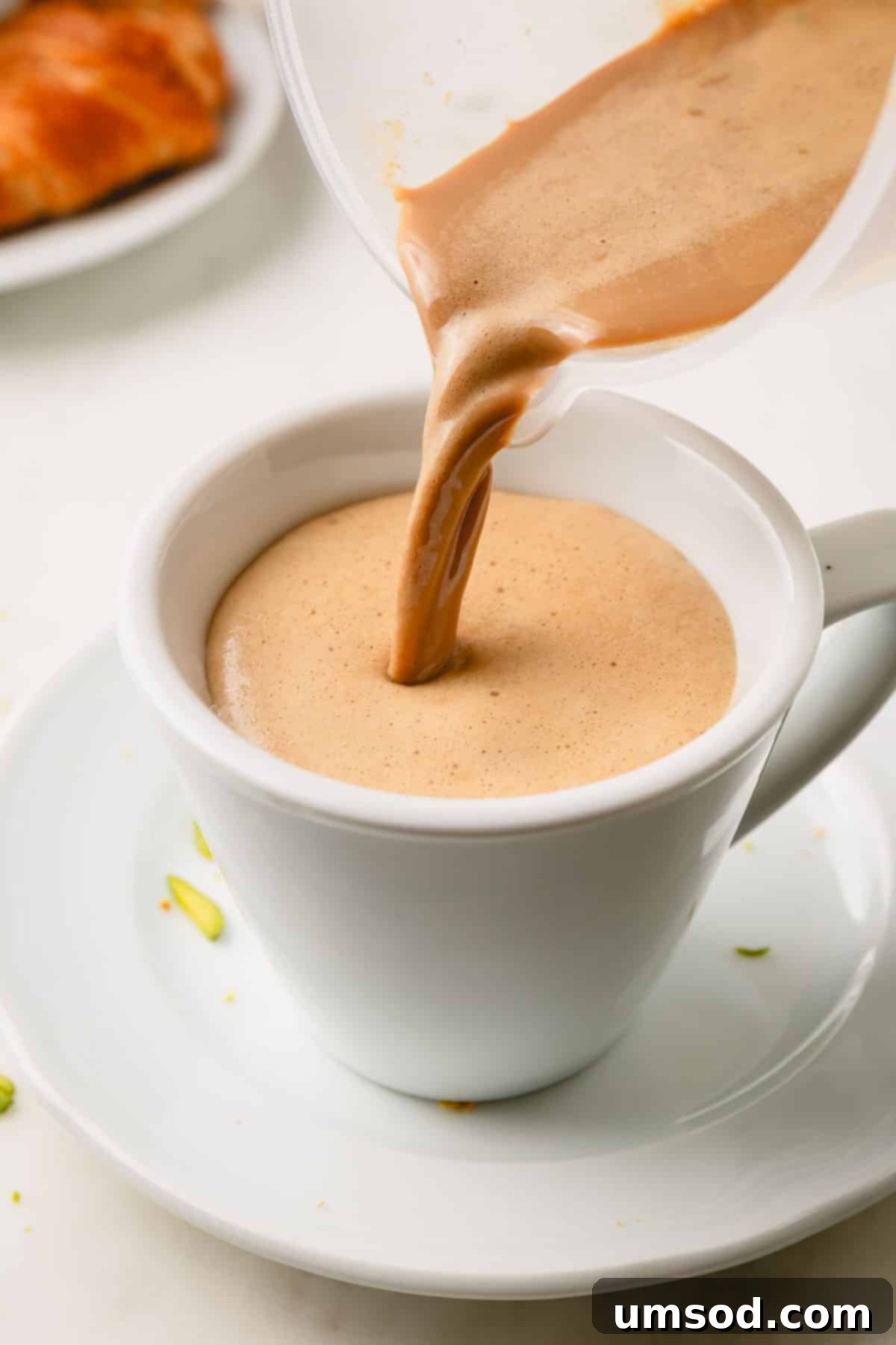 A homemade pistachio latte being poured into an elegant glass mug, ready to be enjoyed.