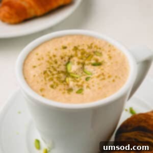 A pistachio latte topped with crushed pistachios on a plate with a croissant.