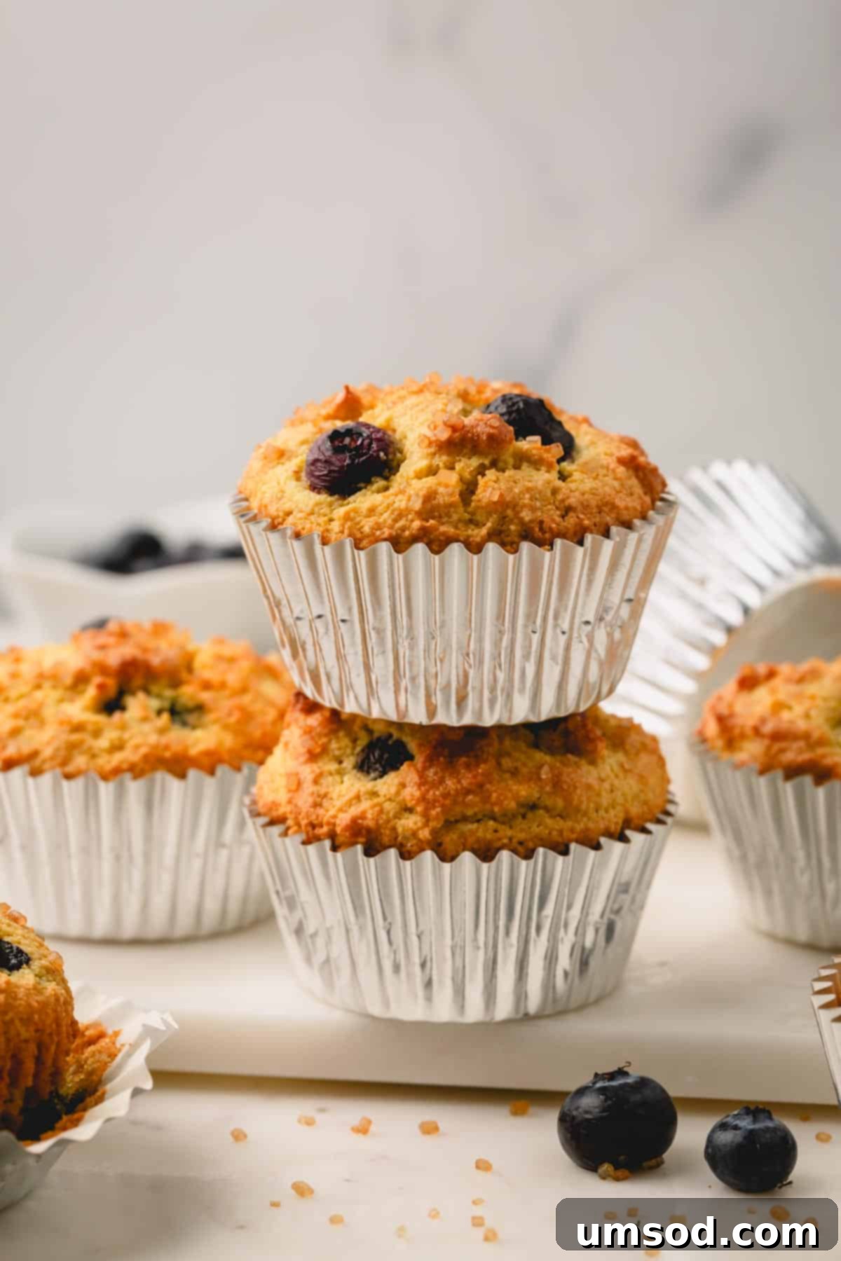 Tender Almond Flour Blueberry Muffins 2 A stack of two almond flour blueberry muffins in muffin liners.