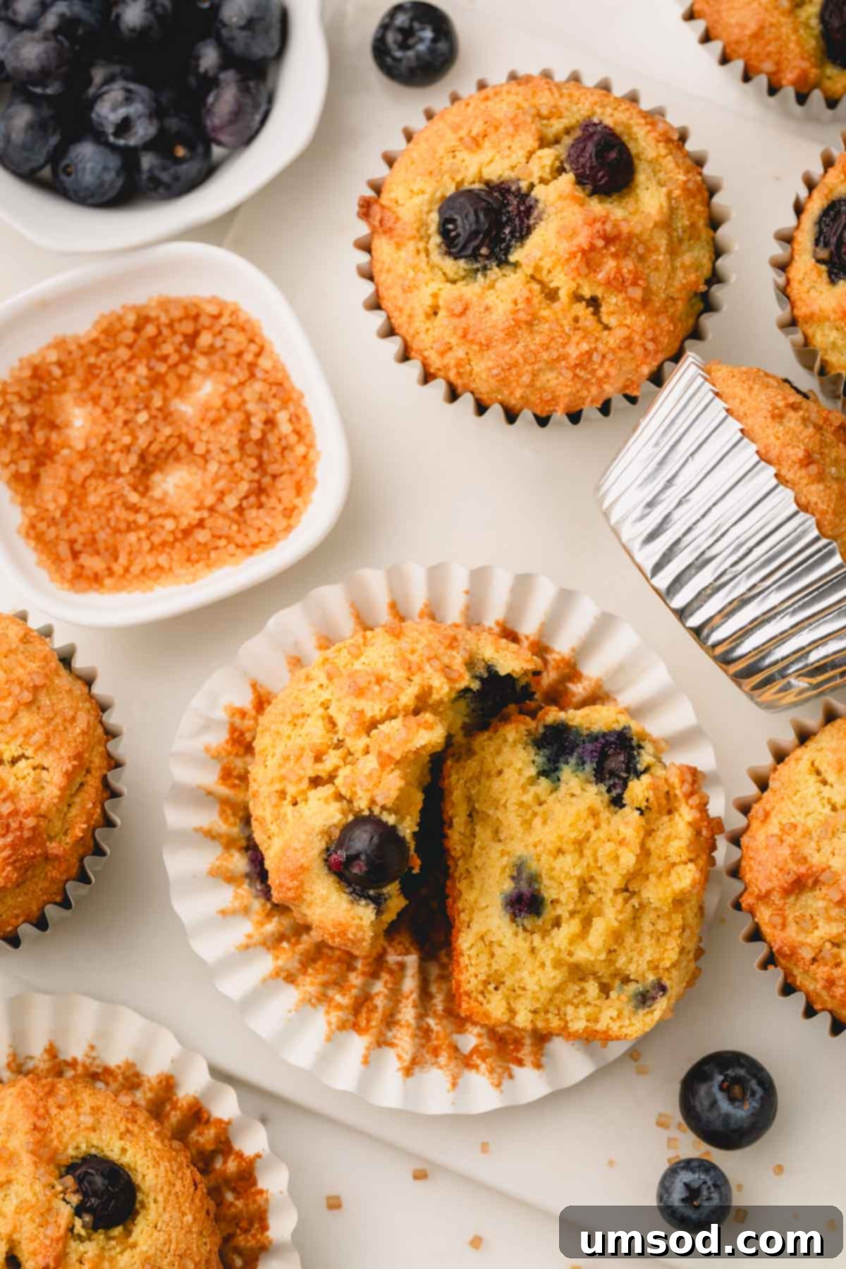 Tender Almond Flour Blueberry Muffins 3 An almond flour blueberry muffin split in half on top of a muffin liner surrounded by other muffins.