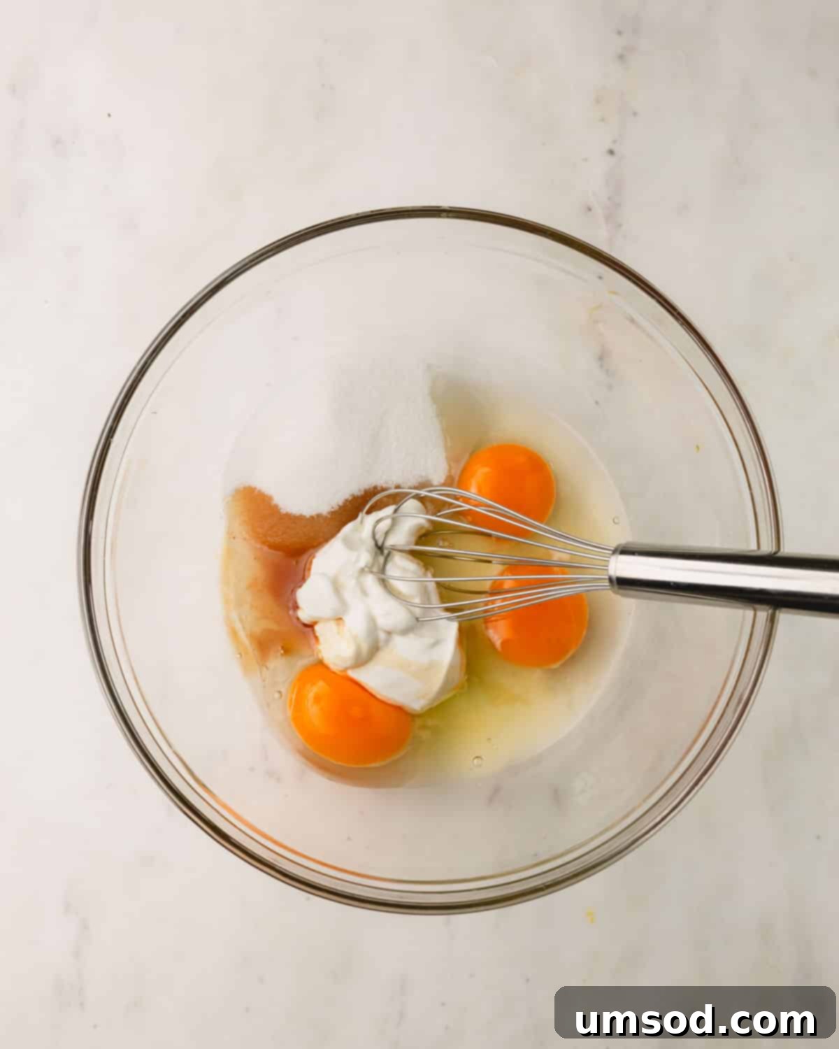 Tender Almond Flour Blueberry Muffins 5 Eggs, sugar, sour cream, and vanilla being whisked in a mixing bowl.