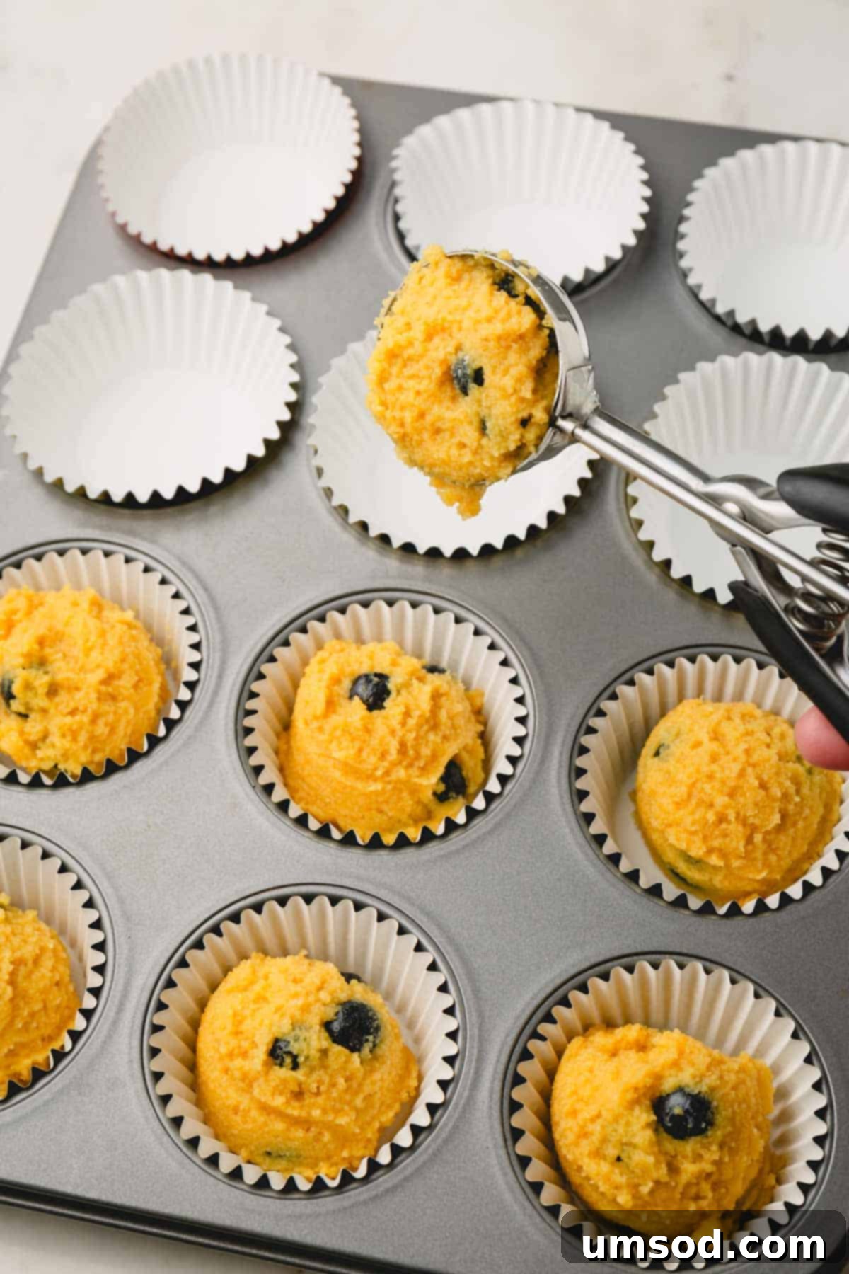 Tender Almond Flour Blueberry Muffins 10 Almond flour blueberry muffin batter being portioned into a muffin tin lined with muffin liners.
