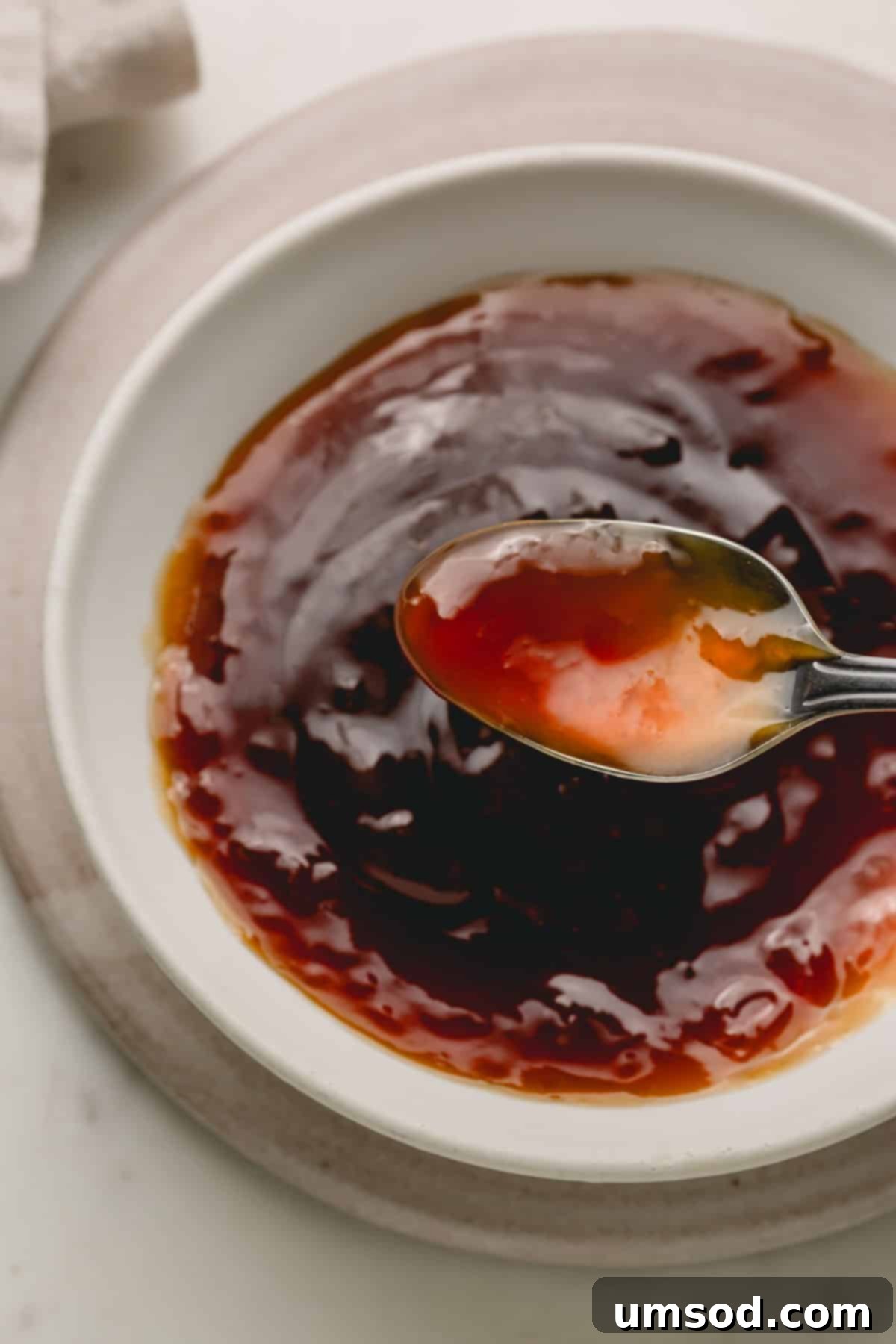 A spoon lifting a scoop of glistening homemade honey teriyaki sauce from a ceramic bowl, showcasing its perfect consistency.