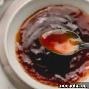 A spoon lifting a scoop of honey teriyaki sauce from a bowl.