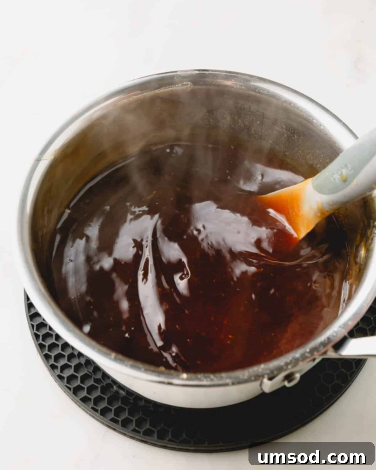 A pot of rich, golden honey teriyaki sauce being gently stirred with a whisk, showing its thick and glossy texture.