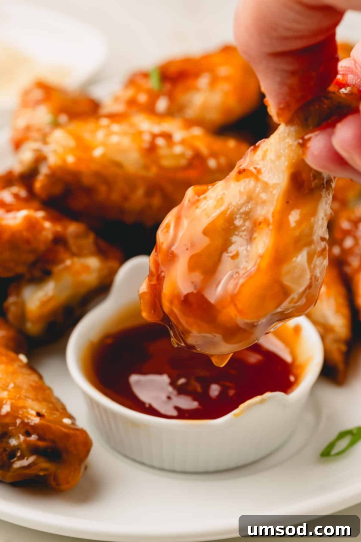 A perfectly cooked chicken wing being generously dipped into a small ramekin of warm, homemade honey teriyaki sauce.