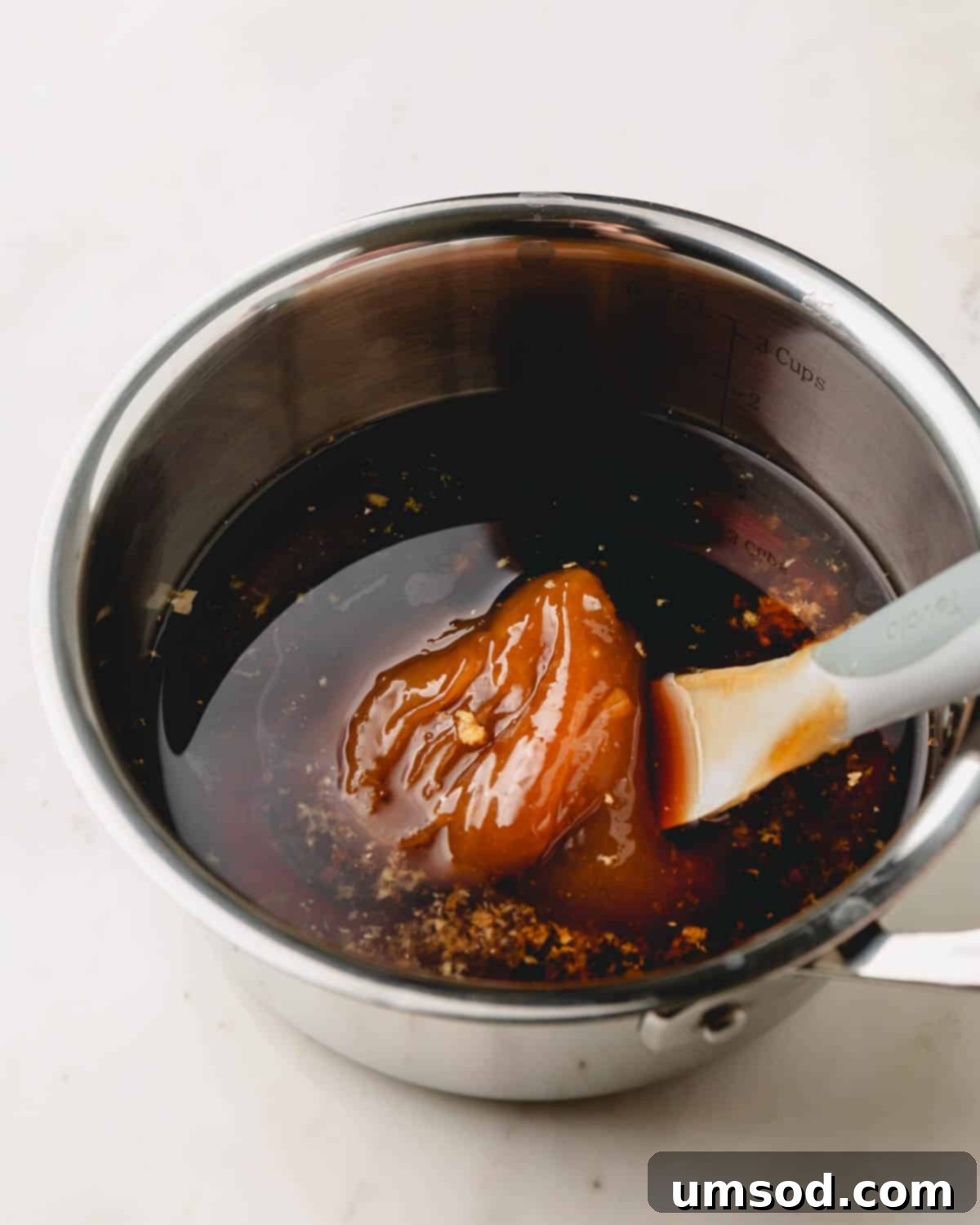 Honey being stirred into a pot of simmering teriyaki sauce with a whisk, ensuring full dissolution.