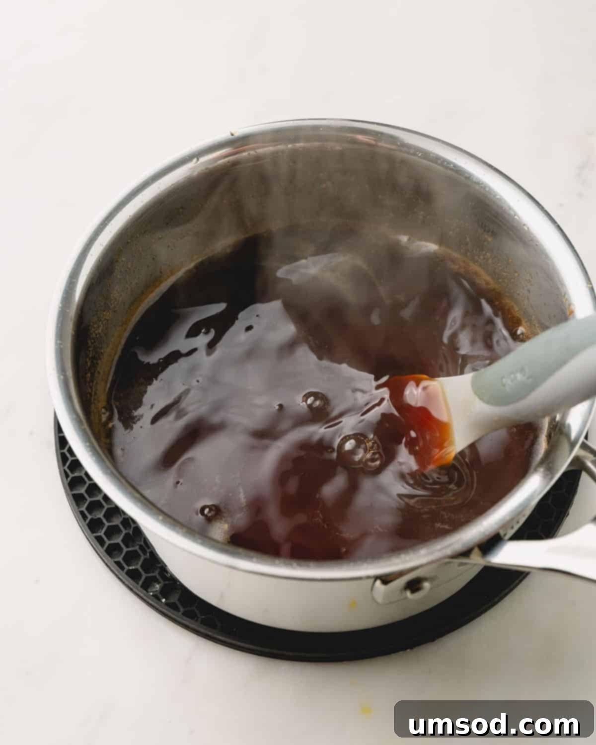 A pot of honey teriyaki sauce gently simmering on the stovetop, showing small bubbles on the surface.