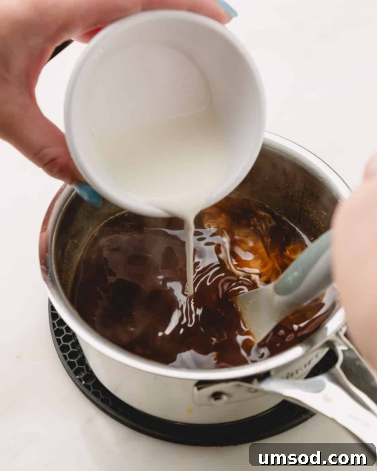 A stream of white cornstarch slurry being poured into a pot of bubbling honey teriyaki sauce, while being continuously whisked.