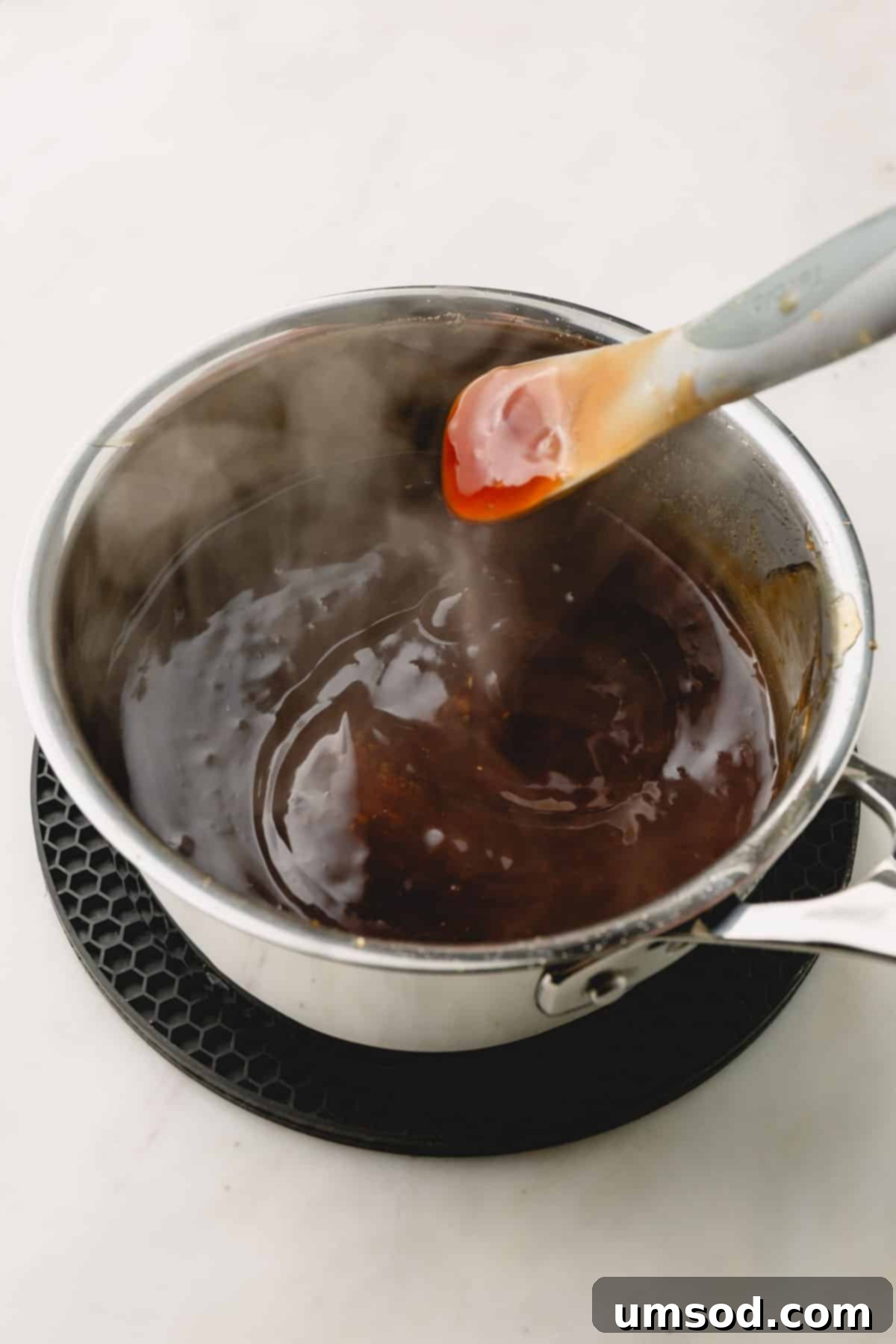 A whisk vigorously stirring glossy honey teriyaki sauce in a saucepan on the stovetop as it thickens.