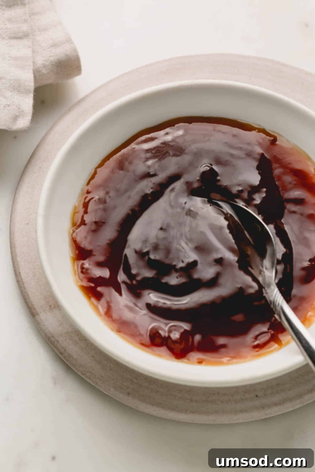 A rustic ceramic bowl filled with glossy honey teriyaki sauce, with a wooden spoon resting inside, ready for serving.