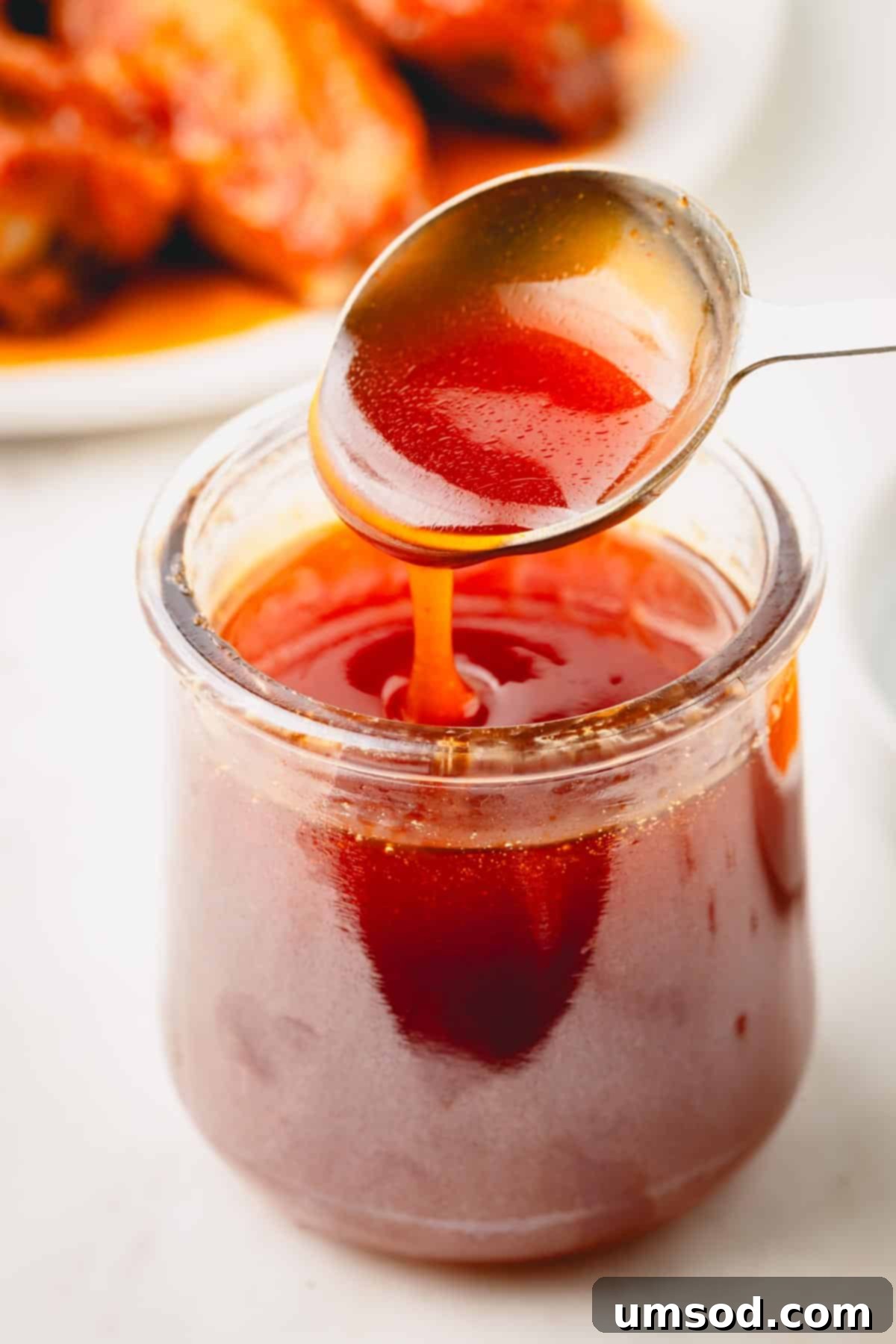 A spoon lifting a scoop of hot honey sauce from a jar, showcasing its rich texture and color.