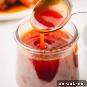 A spoon lifting a scoop of hot honey sauce from a jar, highlighting the rich texture.