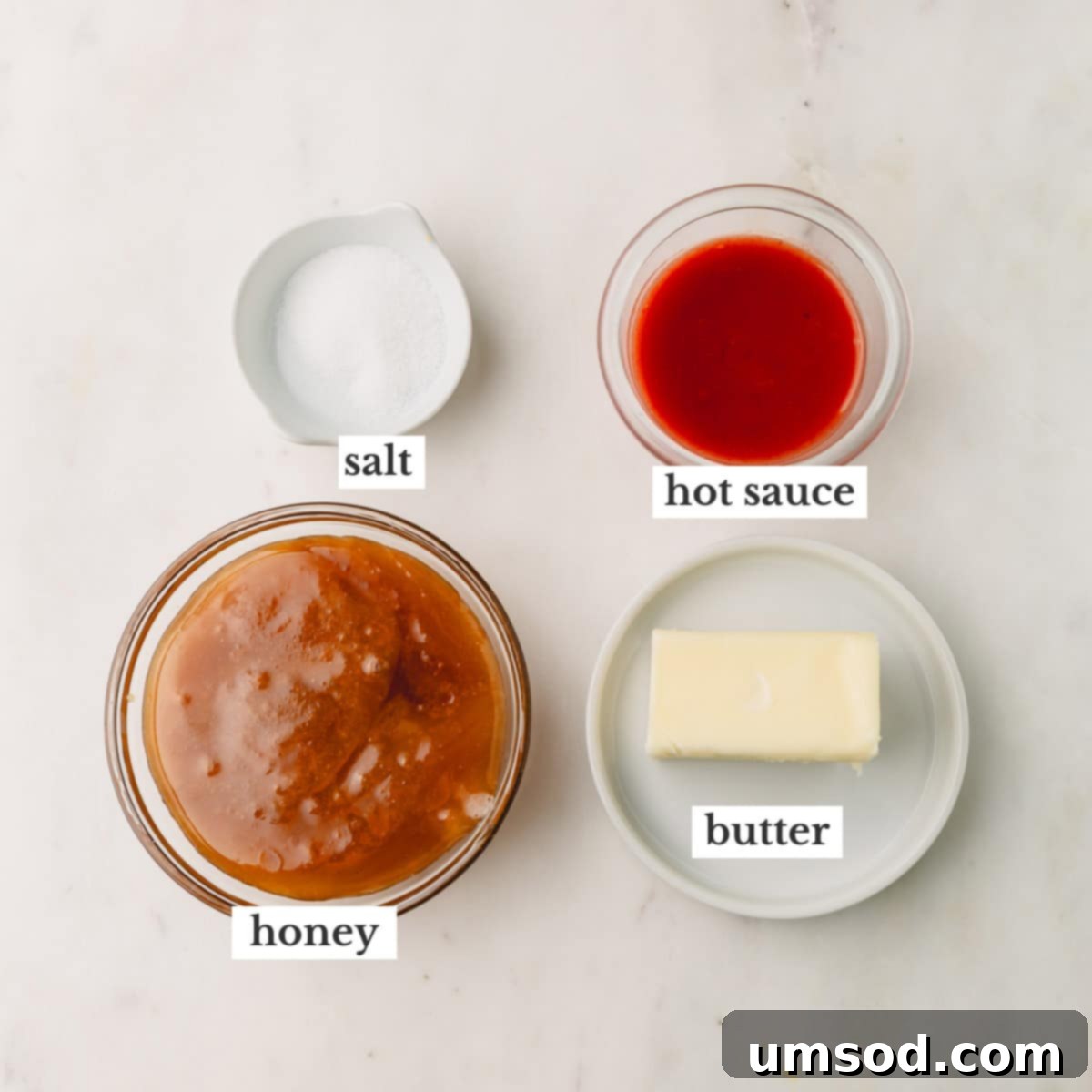 Individual ingredients for hot honey sauce: a block of butter, a jar of honey, a bottle of hot sauce, and a small pile of salt.