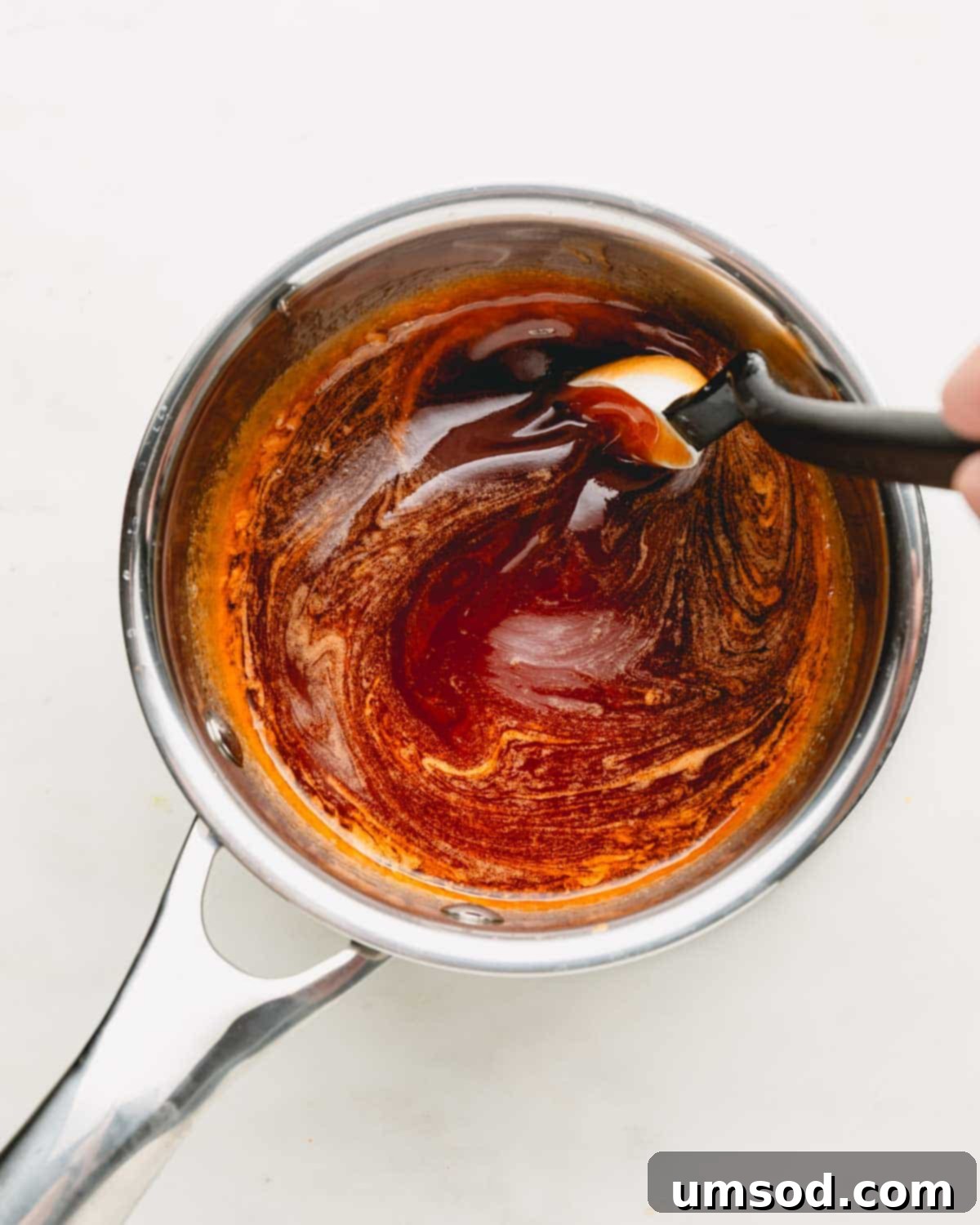 Hot honey sauce being stirred in a pot, showing a smooth, glossy texture.