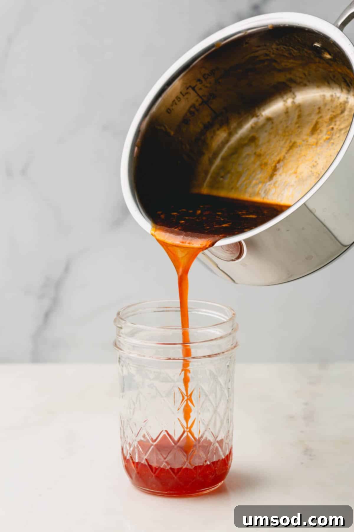 Warm hot honey sauce being poured from a pot into a clear mason jar for storage or immediate use.