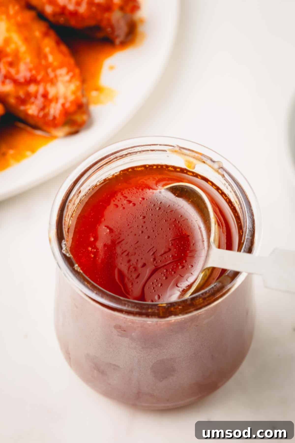 A wooden spoon sticking out of a glass jar of hot honey sauce, ready for serving.