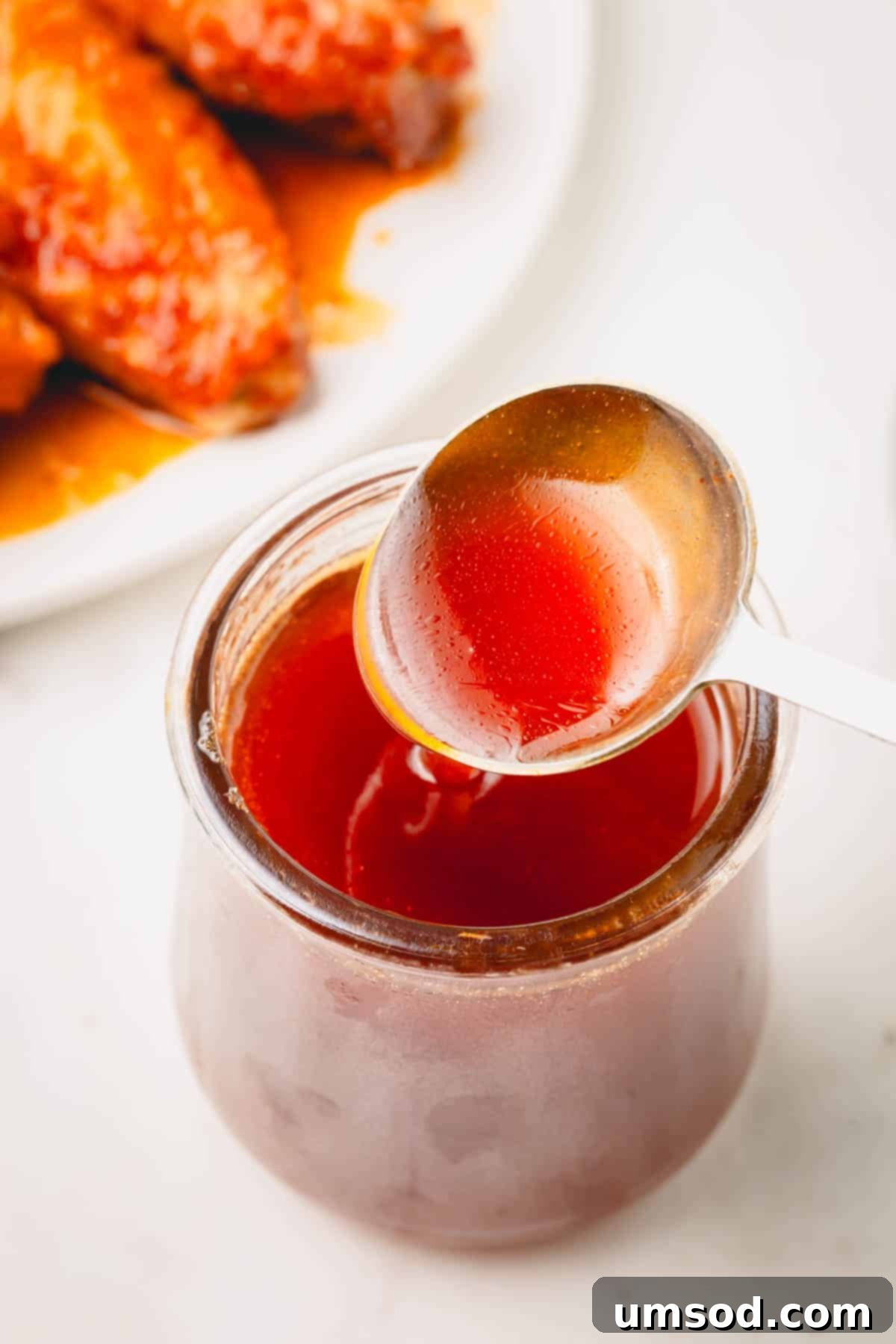 A spoon lifting a scoop of hot honey sauce from a glass jar, showing its glossy texture.