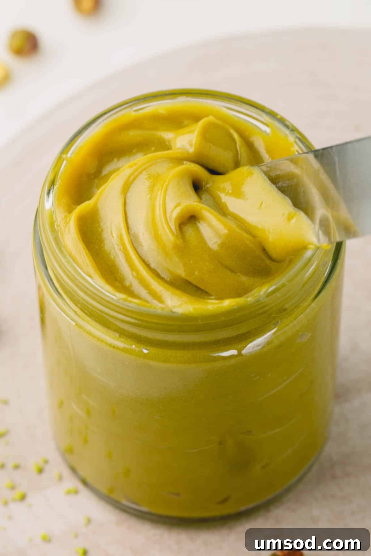 A jar of homemade pistachio butter with a knife sticking out, showcasing its vibrant green color.