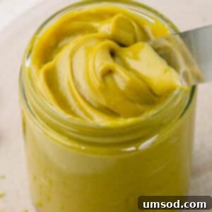 A jar of homemade pistachio butter with a knife sticking out.