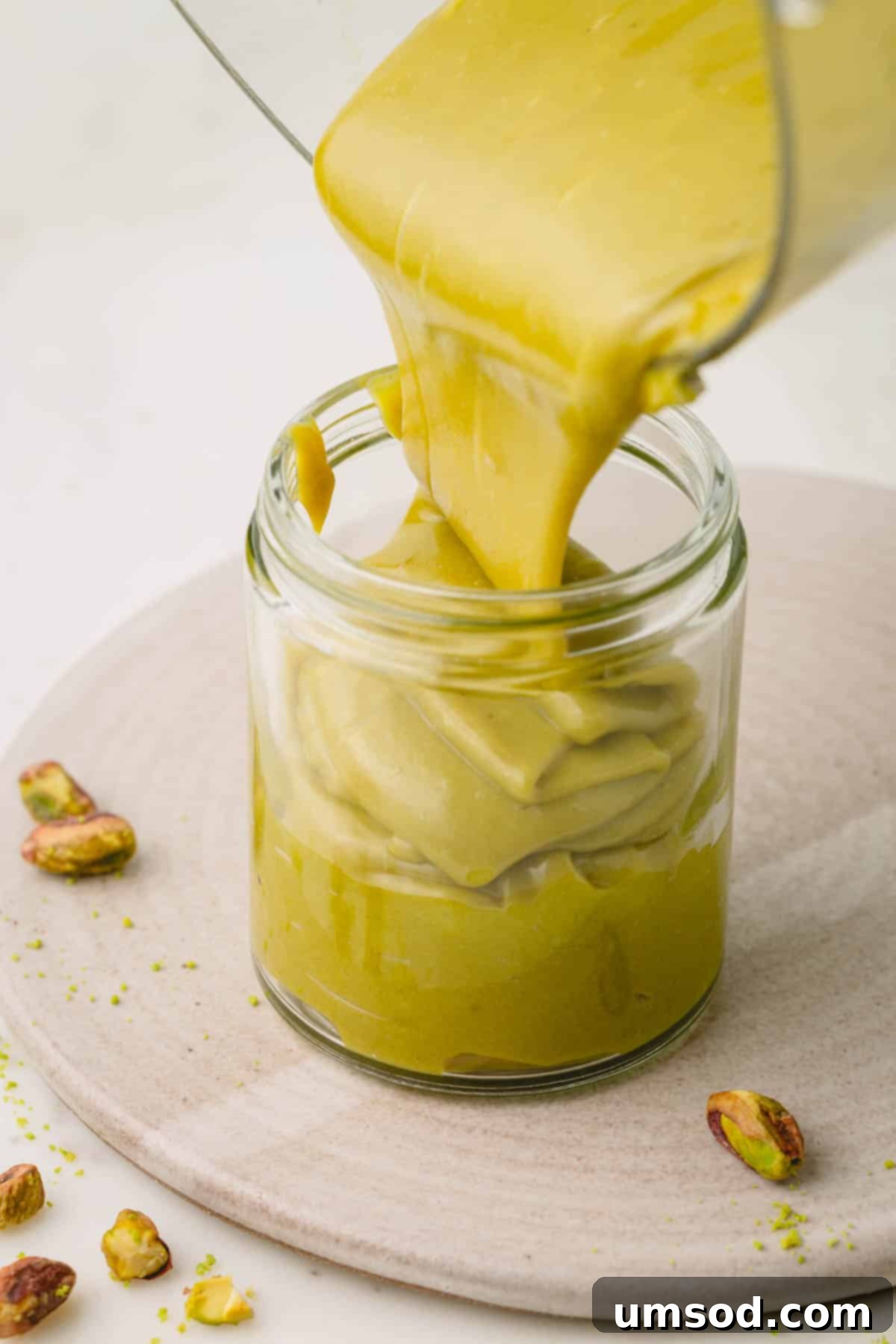 Smooth homemade pistachio butter being poured into a beautiful glass jar, ready for storage.