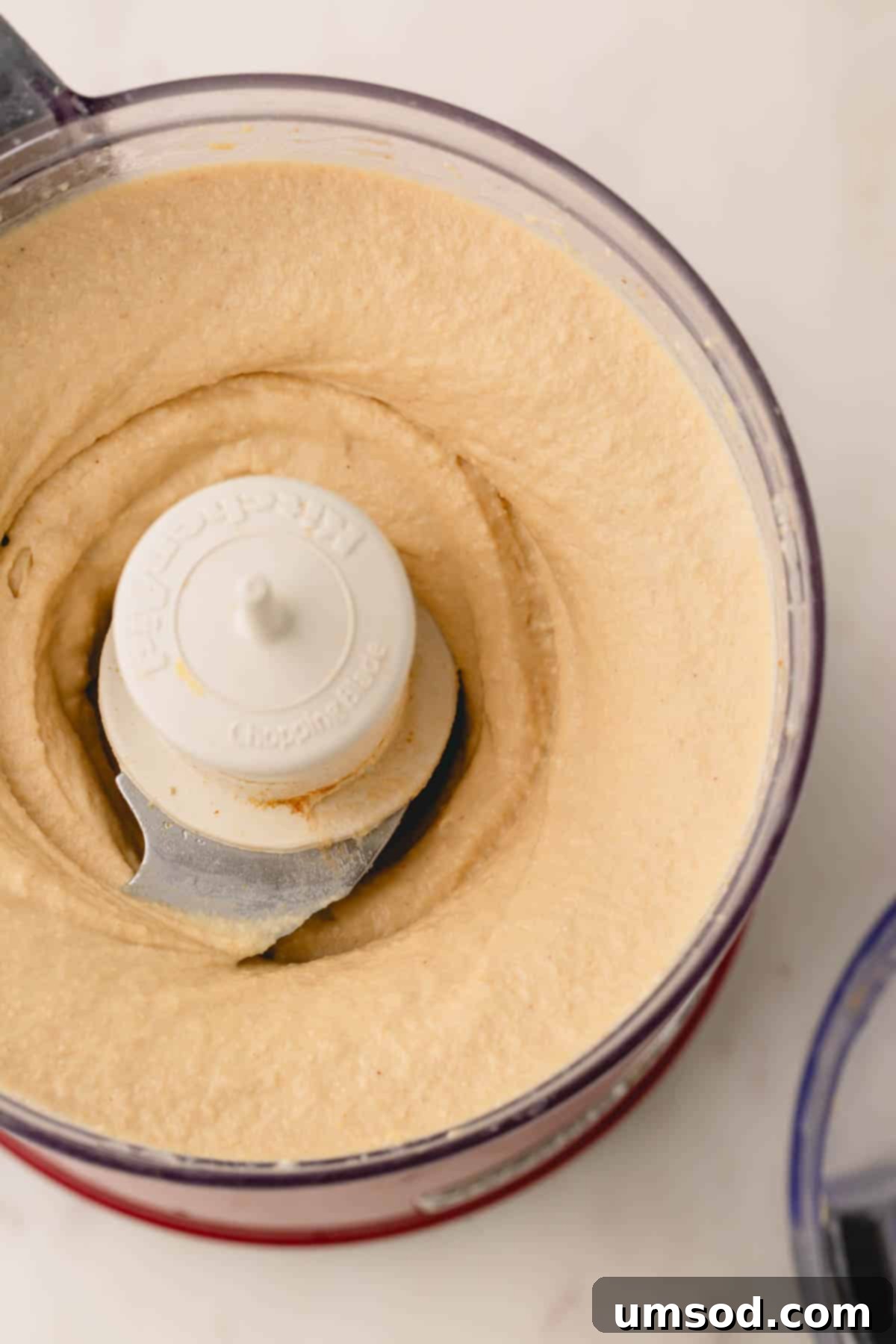 Smooth, perfectly blended roasted garlic hummus filling the bowl of a food processor.
