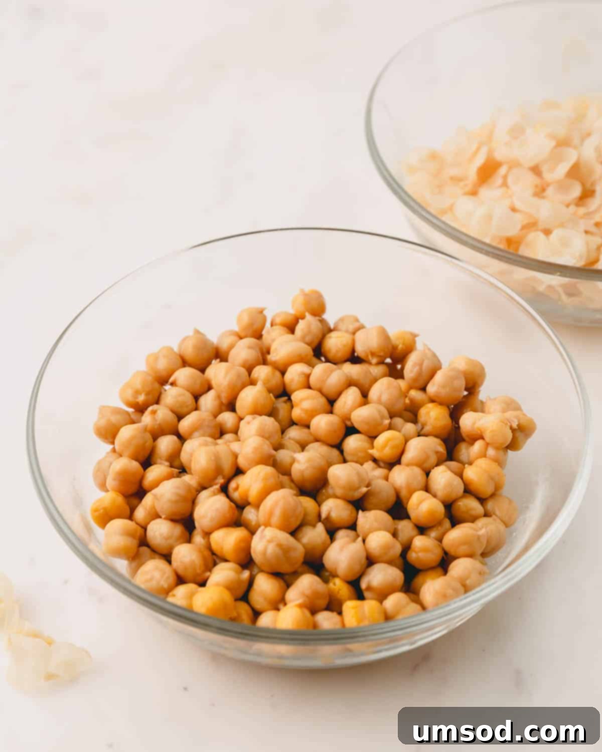 A bowl of freshly peeled chickpeas sits next to a smaller bowl containing the discarded chickpea skins.