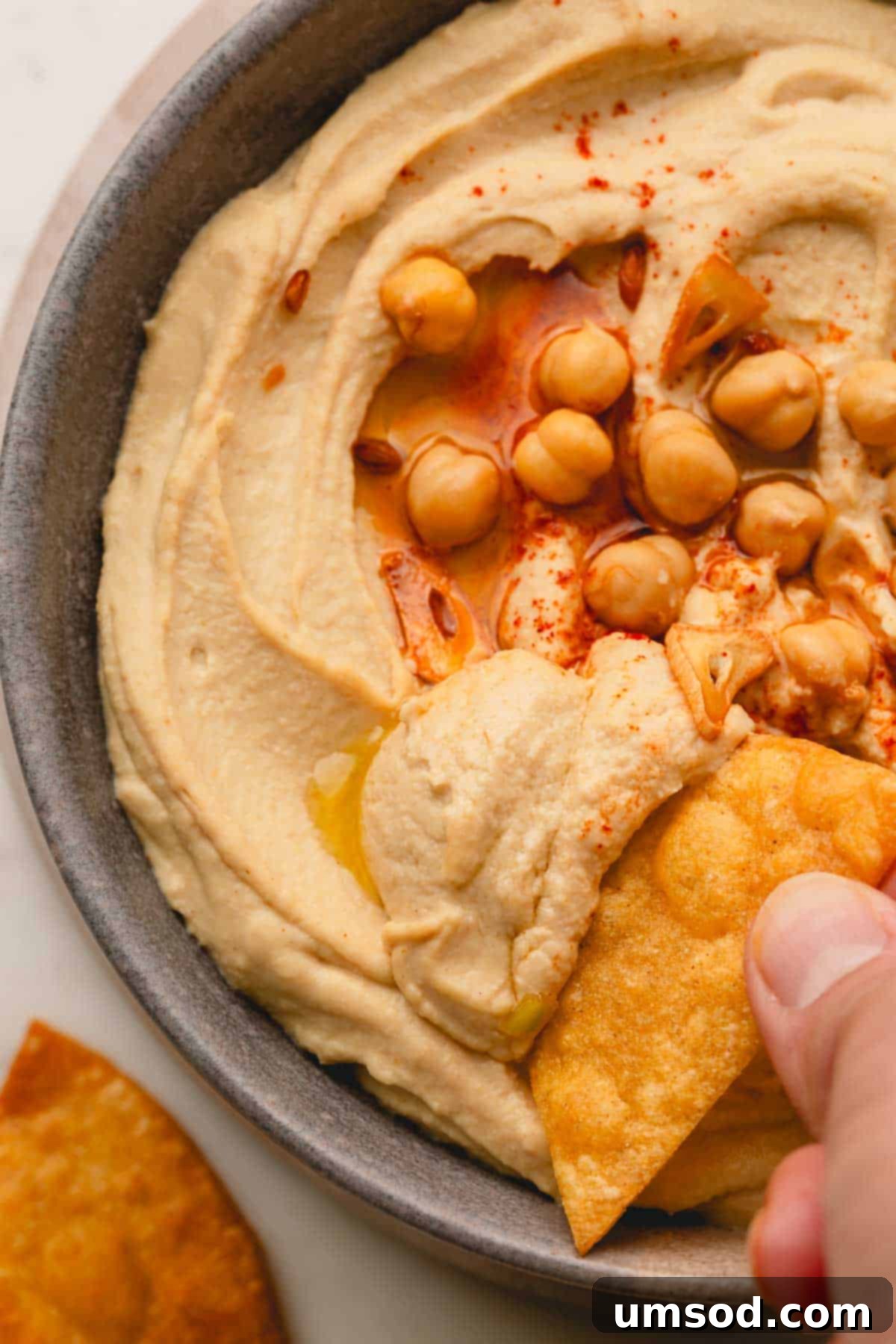 Another enticing shot of a pita chip being dipped into a bowl of rich roasted garlic hummus, garnished with paprika.