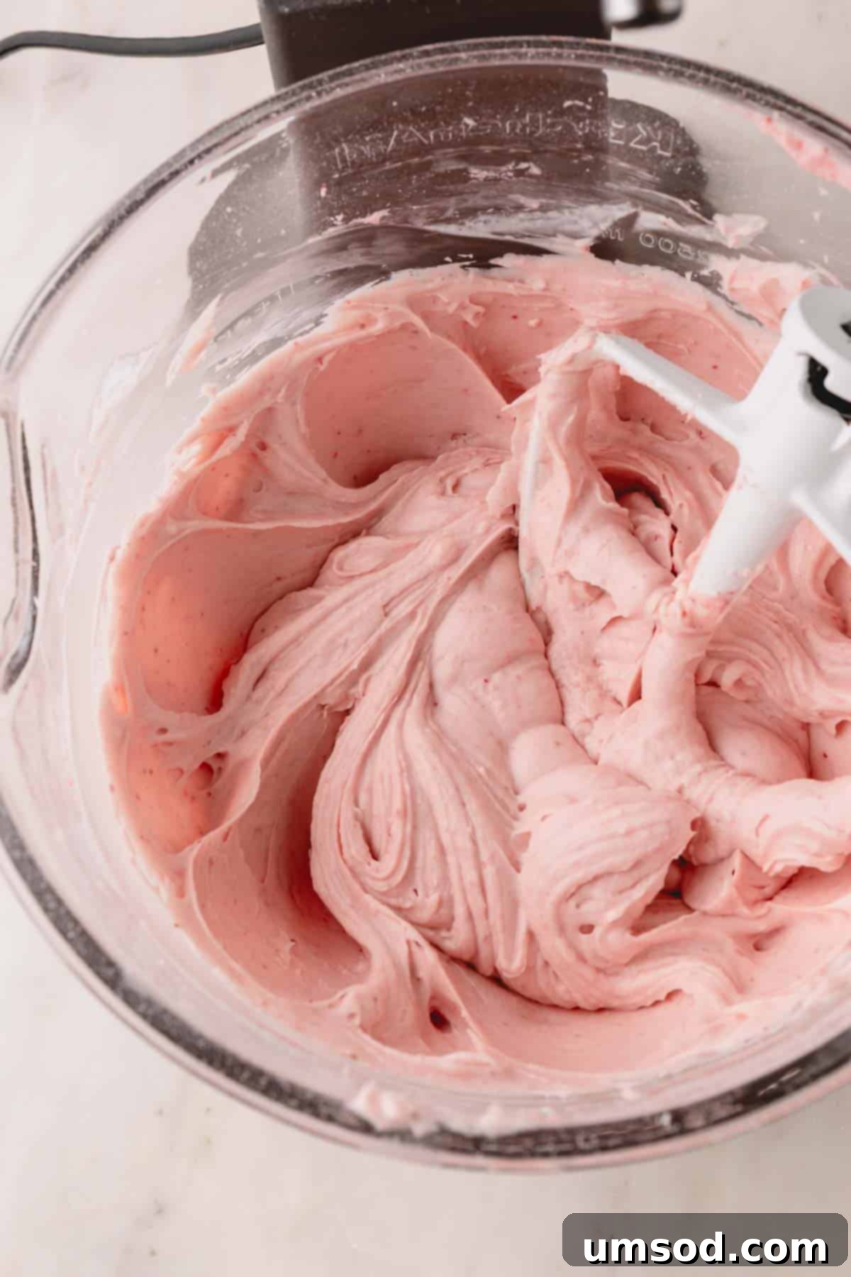 A bowl of vibrant strawberry cream cheese frosting in a stand mixer, fitted with a paddle attachment.
