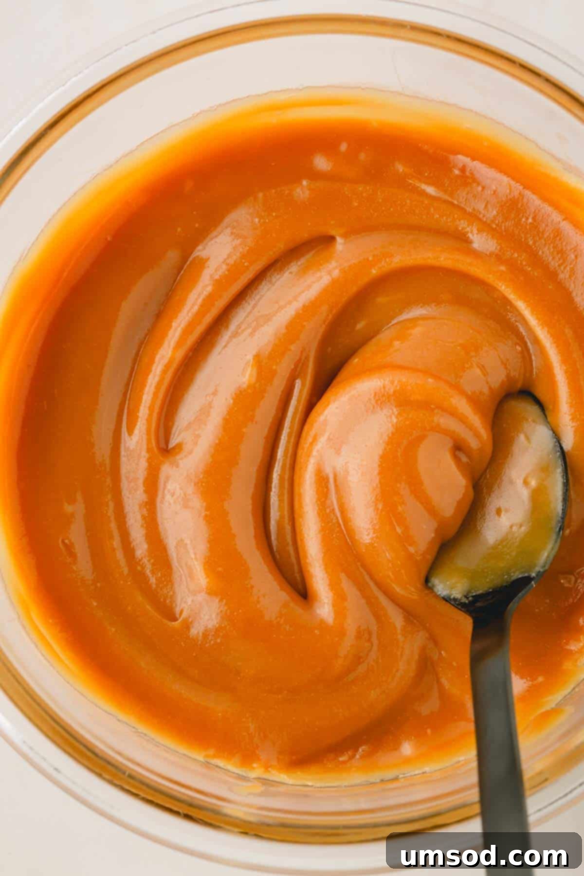 A spoon swirling creamy vegan caramel filling in a bowl, showcasing its texture.
