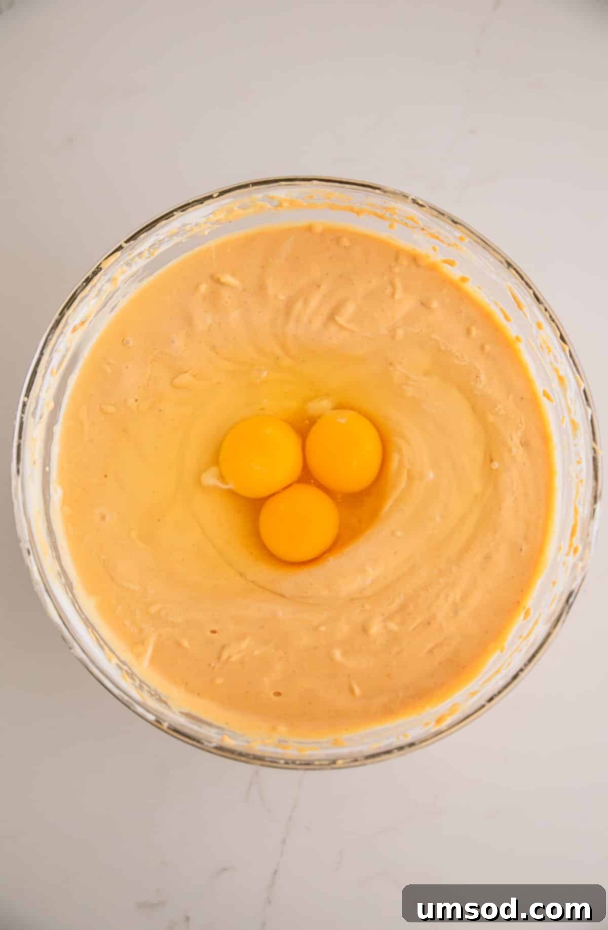 Three eggs in a bowl of maple pumpkin cheesecake filling.