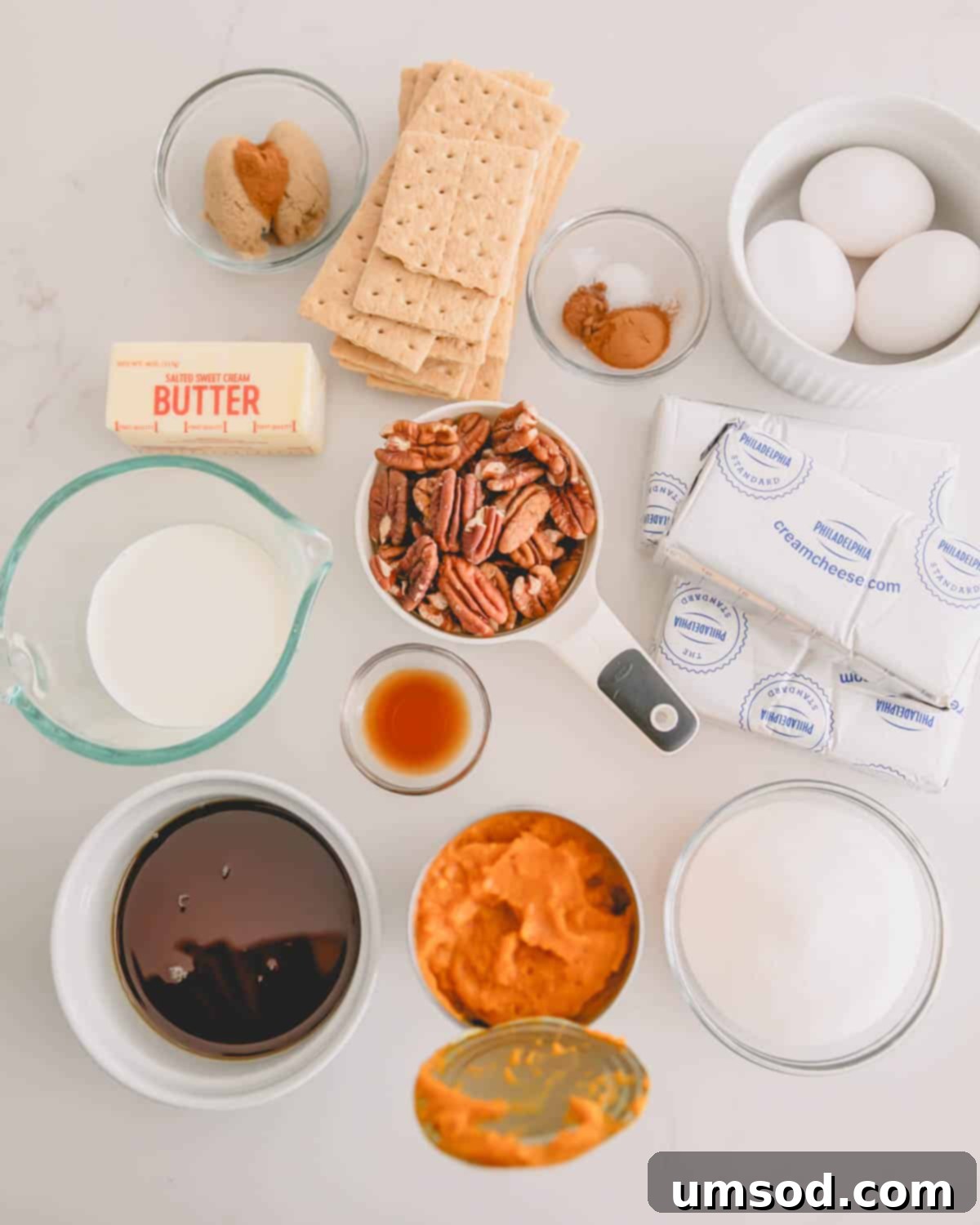 An assortment of ingredients needed to create a delicious maple pumpkin cheesecake with a graham cracker crust.