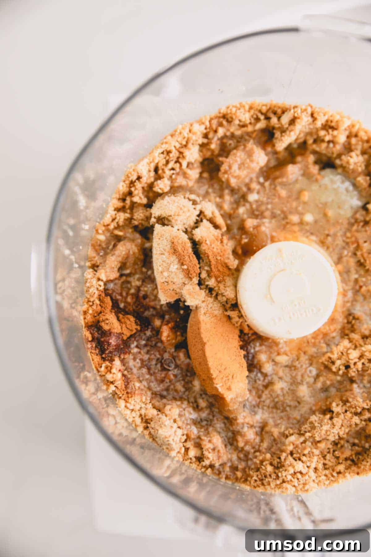A mixture of graham cracker crumbs, melted butter, and spices in a food processor.