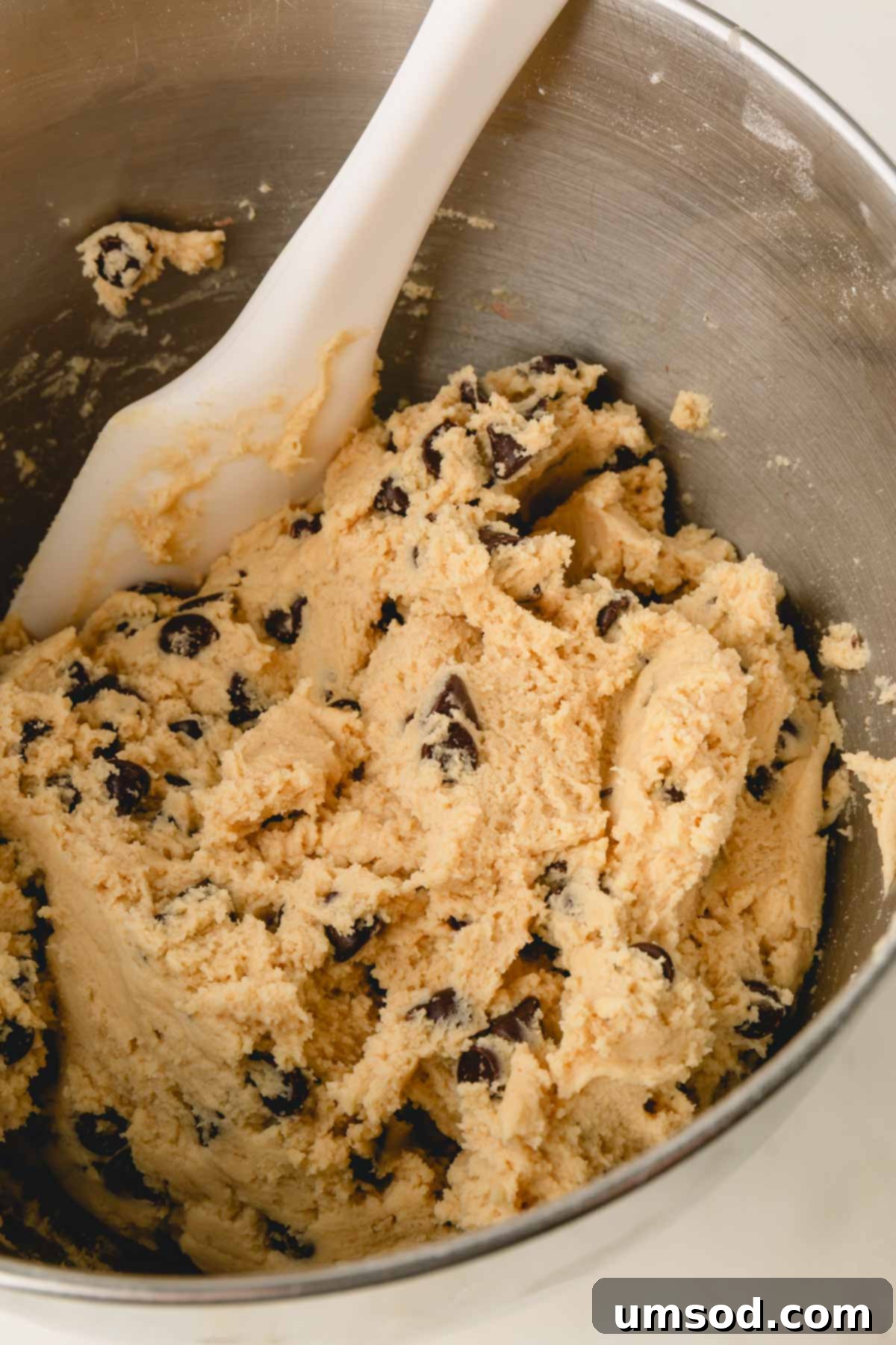 Chocolate chip cookie dough being mixed with a spatula in a bowl.