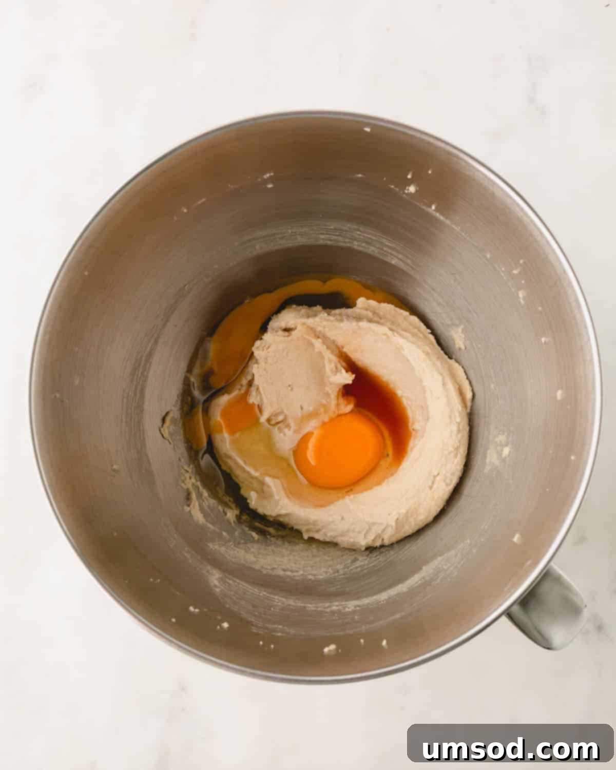 Eggs and vanilla extract being added to cookie dough in a mixing bowl.