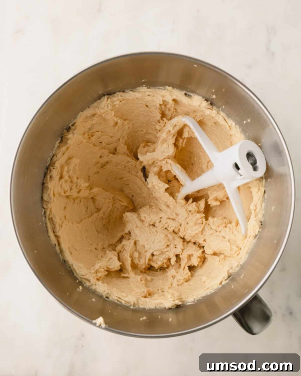 Cookie dough being mixed in a bowl with a whisk attachment.