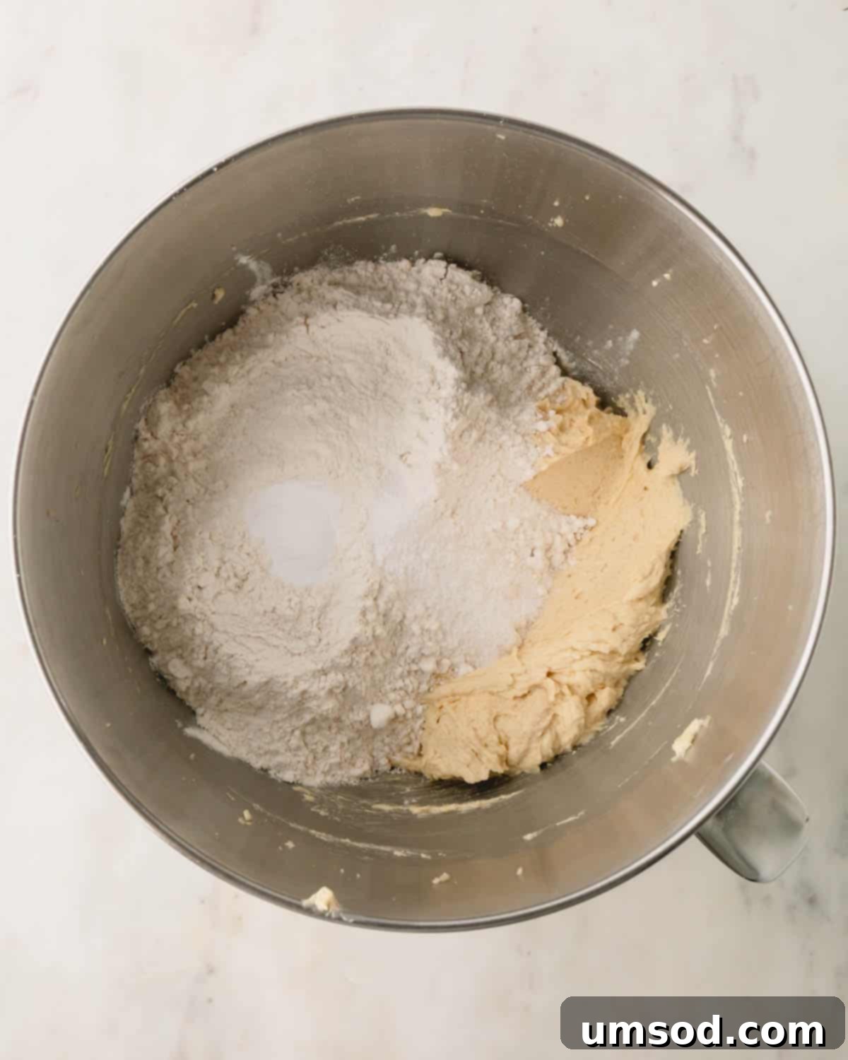 Dry ingredients being added to cookie dough in a mixing bowl.