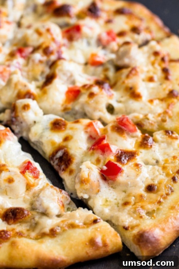 Close-up of creamy cheesy chicken alfredo topping on a homemade thin crust pizza