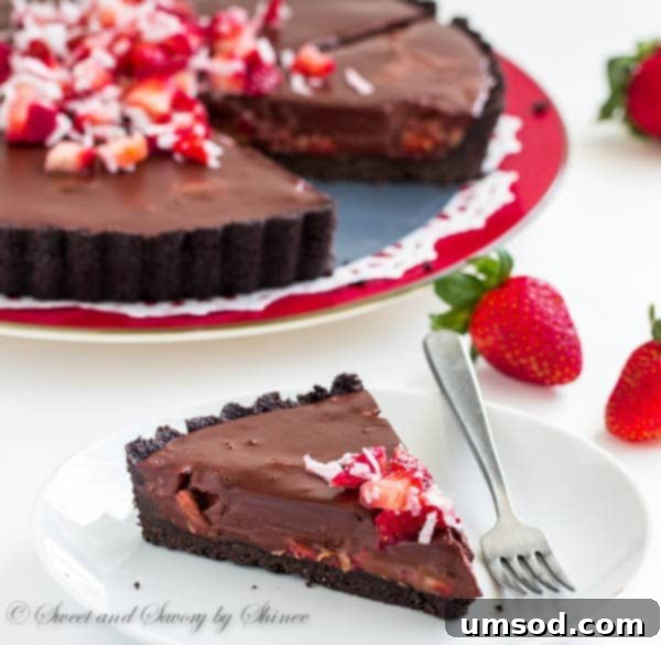 Close-up of a slice of chocolate truffle tart showcasing the layers of rich ganache, fresh strawberries, and coconut.