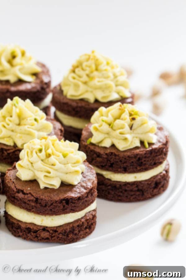 A cross-section view of a mini chocolate layer cake, revealing the moist chocolate cake layers and the thick, green pistachio buttercream filling.