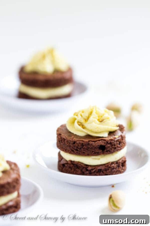 Several mini chocolate layer cakes arranged on a cooling rack, freshly frosted with pistachio buttercream and sprinkled with chopped pistachios.