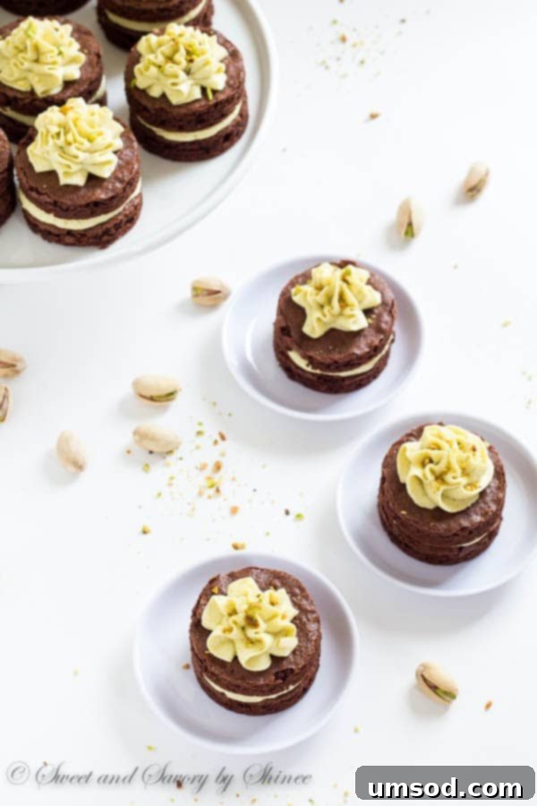 A close-up shot of a finished mini chocolate layer cake, artfully decorated with piped pistachio buttercream and finely chopped pistachios, ready for enjoyment.