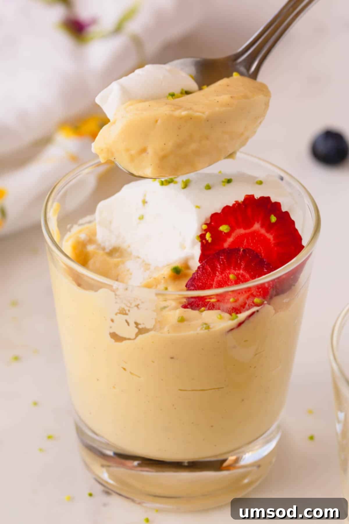 A spoon lifting a scoop of vanilla pudding from a cup.