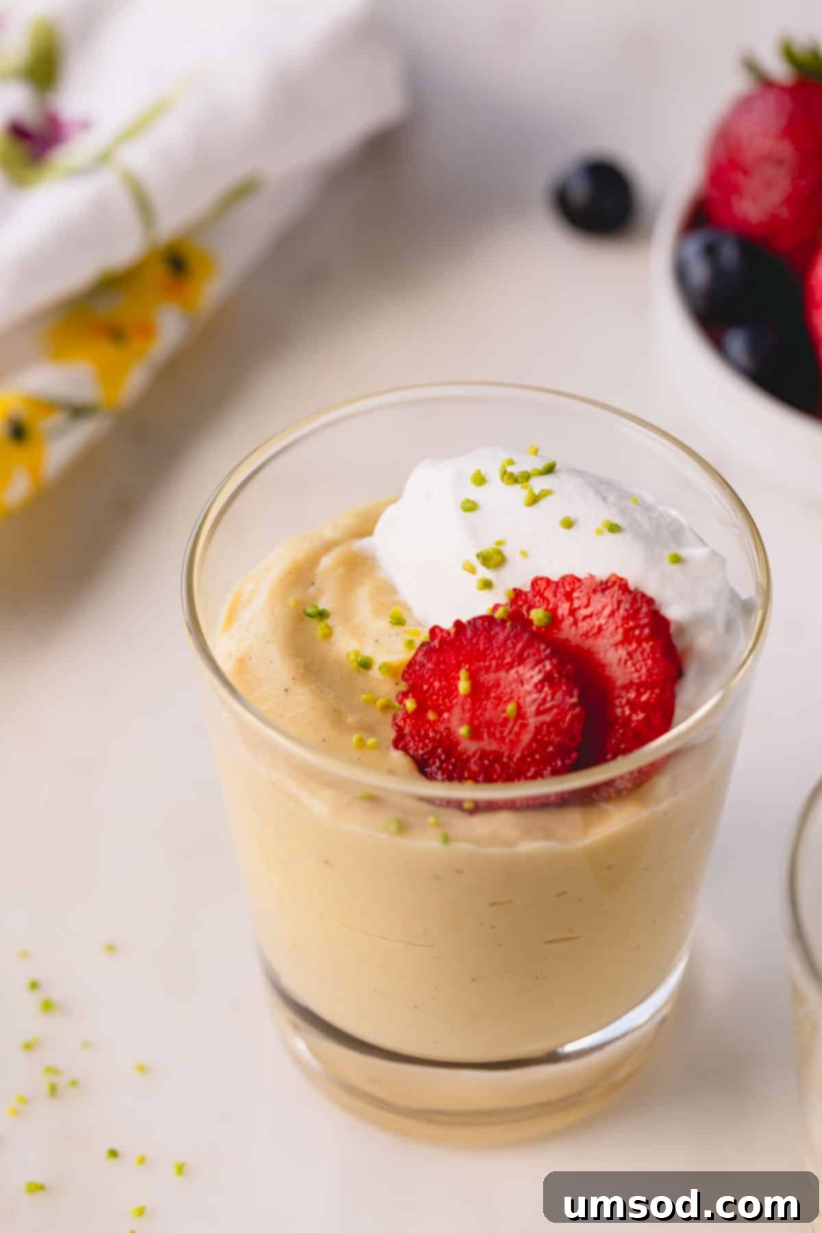 A cup of vanilla pudding topped with strawberries, whipped cream, and crushed pistachios.