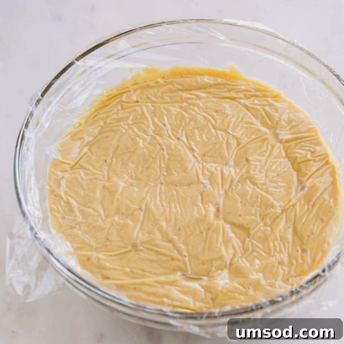 A bowl of vanilla pudding with plastic wrap covering the top.