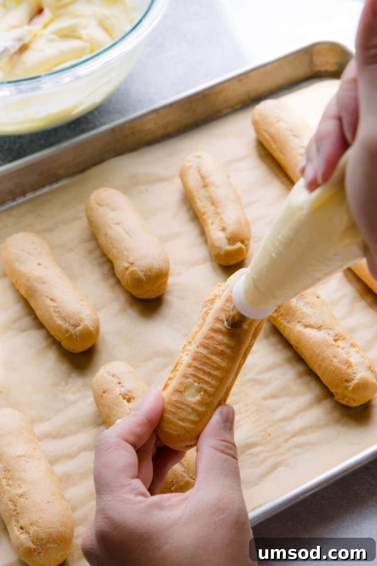 Decadent Chocolate Eclairs 11 A hand demonstrating the filling of an eclair shell by inserting a piping bag into a hole on the bottom.