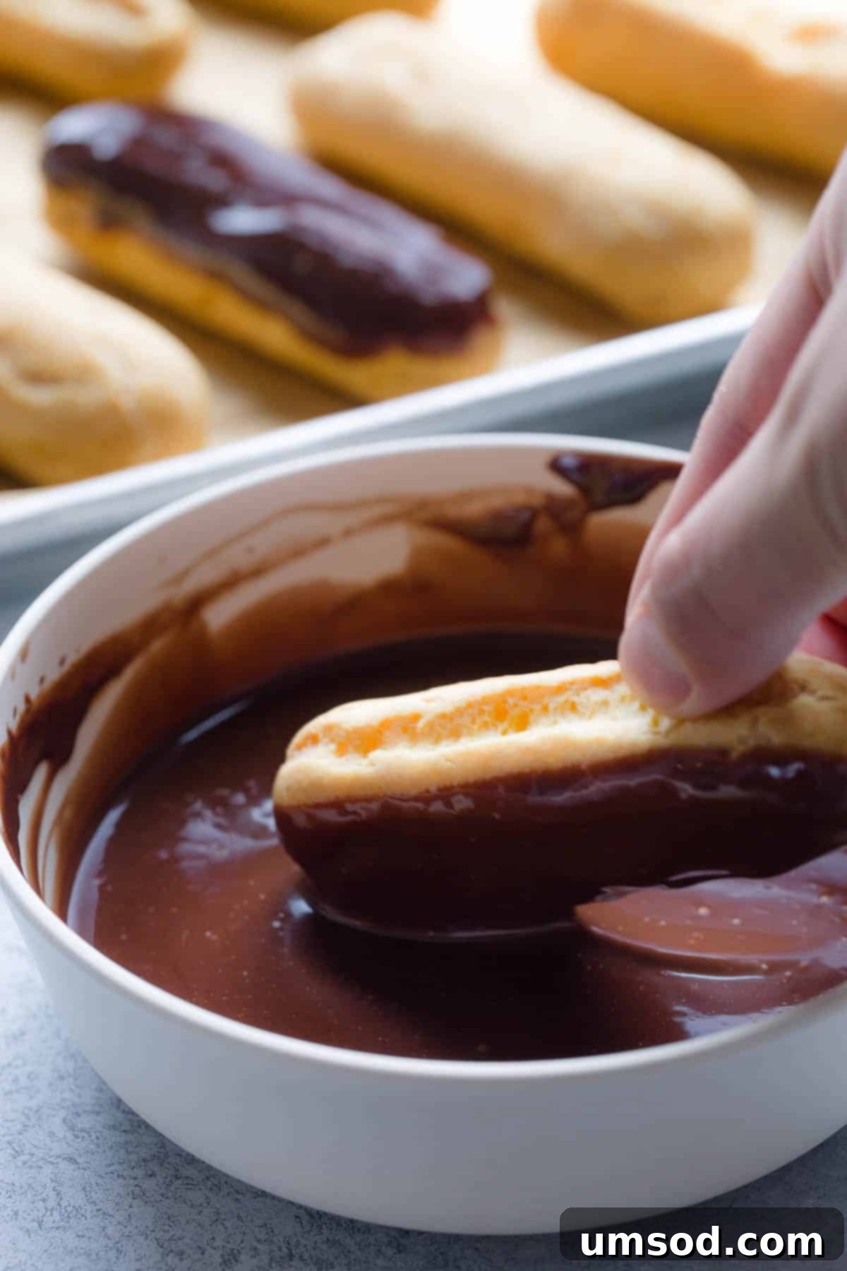 Decadent Chocolate Eclairs 12 A filled eclair being expertly dipped into a bowl of smooth, glossy chocolate ganache.